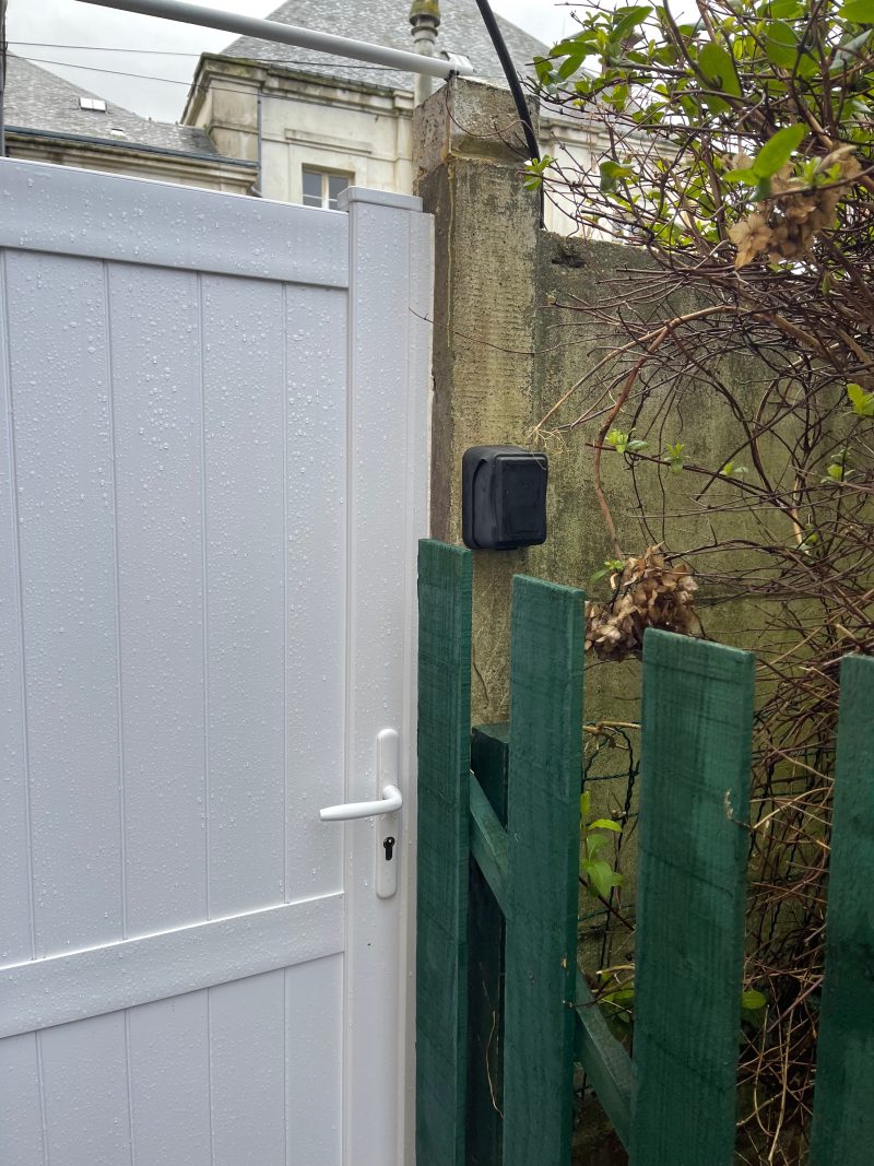 Boite à clés posée devant une porte de jardin